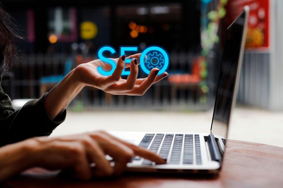 Femme devant un ordinateur portable qui tient dans sa main gauche le mot "SEO" en bleu et tape sur une touche de son clavier avec la main droite